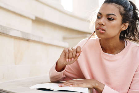 Image of thinking african american student girl doing homework with laptop while sitting on stairs outdoorsの写真素材