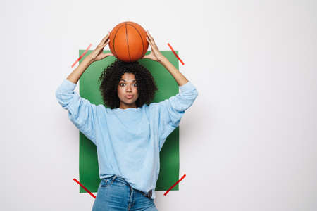 Image of surprised african american woman posing with basketball on her head isolated over multicolored backgroundの写真素材