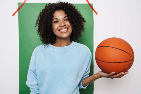 Image of pleased african american woman smiling while posing with basketball isolated over multicolored backgroundの写真素材