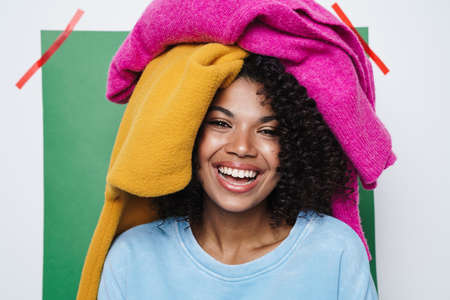 Image of cheerful african american woman laughing with clothes on her head isolated over multicolored backgroundの写真素材