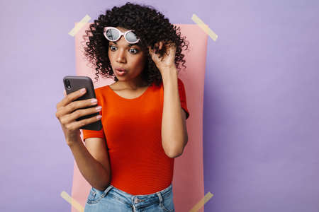 Image of surprised african american woman using mobile phone isolated over multicolored background
