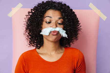 Image of amusing african american woman making fun with cotton candy isolated over multicolored backgroundの写真素材