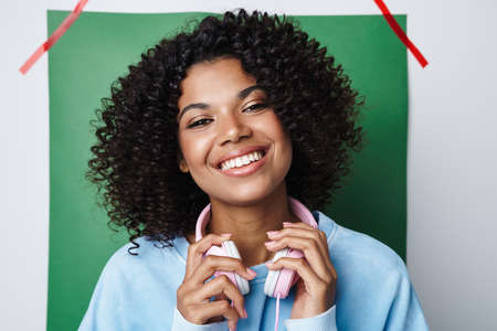 Image of joyful african american woman with headphones smiling at camera isolated over multicolored backgroundの写真素材