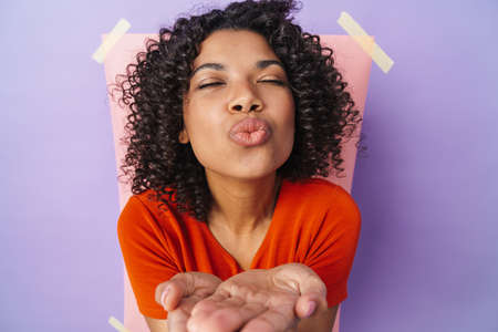 Image of happy african american woman blowing air kiss at camera isolated over multicolored backgroundの写真素材