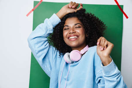 Image of joyful african american woman with headphones smiling and dancing isolated over...