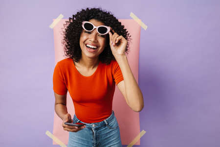 Image of happy african american woman laughing while using cellphone isolated over multicolored...