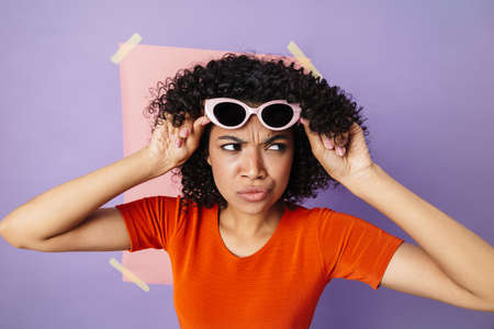 Image of displeased african american woman in sunglasses looking aside isolated over multicolored...