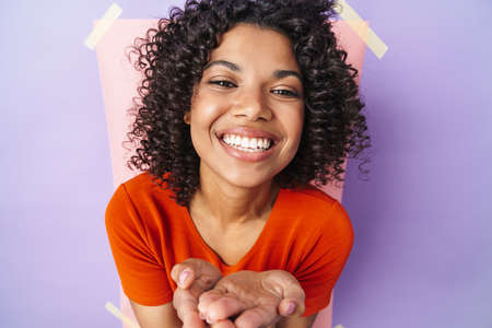 Image of funny african american woman smiling and holding copspace isolated over multicolored...