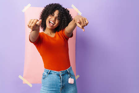 Image of excited african american woman pointing fingers at camera isolated over multicolored...
