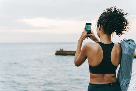 Image of young african american sportswoman taking photo on cellphone at promenadeの写真素材