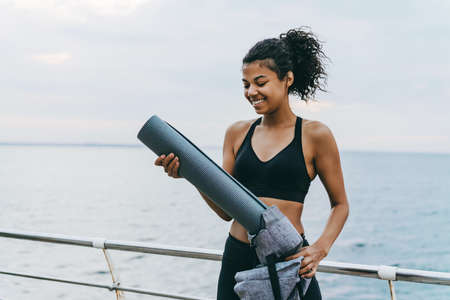 Image of pleased african american sportswoman preparing for workout on promenade