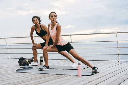 Image of focused multinational sportswomen doing exercise while working out on promenadeの写真素材