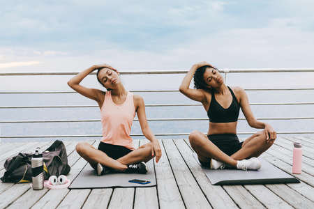 Image of focused multinational sportswomen stretching their necks while working out at promenadeの写真素材