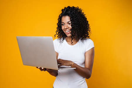 Image of joyful african american woman smiling and using laptop isolated over yellow background