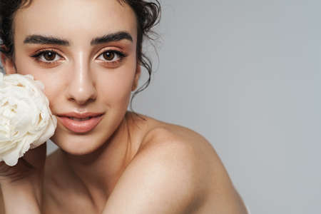 Image of pleased half-naked woman posing with white flower on camera isolated over gray wall
