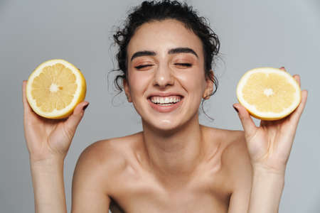 Image of joyful half-naked woman laughing while posing with lemon isolated over gray wallの写真素材