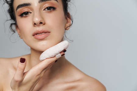 Image of pleased half-naked woman using powder sponge isolated over gray wallの写真素材