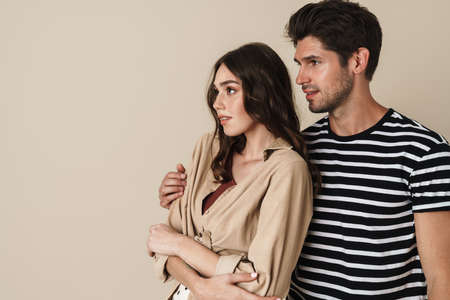 Image of young beautiful couple hugging and posing on camera isolated over beige backgroundの写真素材