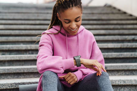 Young smilling fit woman checking smart watch while sitting on stairsの写真素材