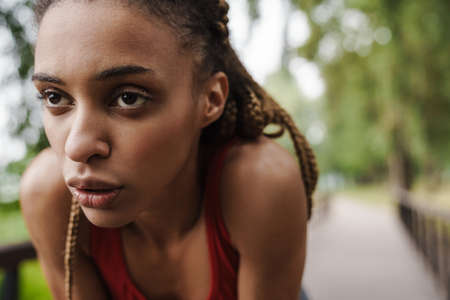 Close up of a tired fit young african woman resting after run in the parkの写真素材