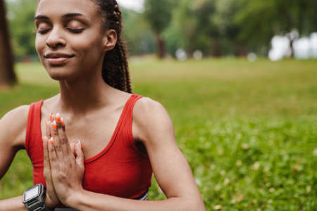 Attractive young african fitness woman sitting in lotus position in park