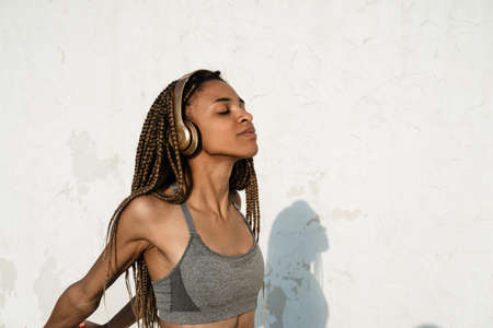 Image of pleased african american girl using headphones while working out outdoorsの写真素材