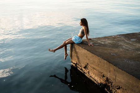 Image of pleased african american girl smiling while sitting on concrete promenade