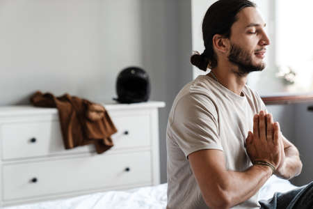 Young man meditating in bedroom in the morningの写真素材