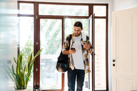 Young man wearing medical mask walking in door using mobile phoneの写真素材