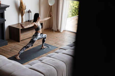 Image of concentrated asian woman in sportswear doing exercise while working out on mat at homeの写真素材