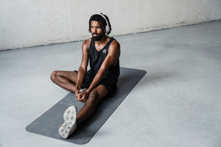 Image of strong african american sportsman in headphones doing exercise while working out on mat...