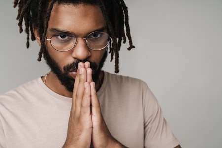 Photo of handsome serious praying african guy isolated over grey wall background in eyeglassesの写真素材