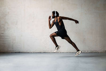 Image of athletic african american sportsman in headphones running while working out indoors