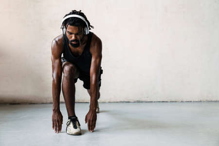 Image of athletic african american sportsman in headphones doing exercise while working out indoors