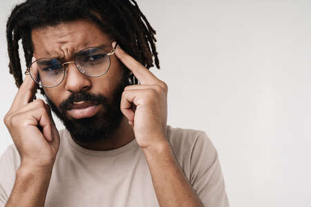 Image of displeased african guy with headache isolated over grey wall background in eyeglassesの写真素材