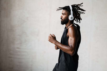 Image of athletic african american sportsman in headphones doing exercise while working out indoorsの写真素材