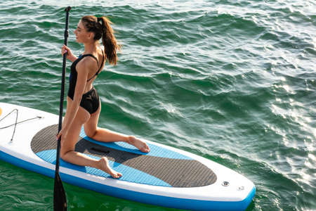 Image of happy beautiful girl in swimsuit smiling and kayaking with paddle on sea
