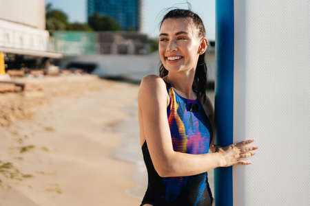 Image of cheerful young beautiful fitness woman outdoors at the beach holding surfboard
