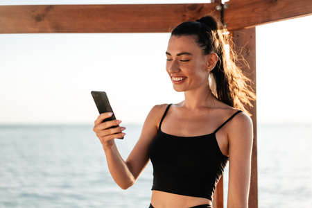 Image of young cheerful girl smiling and taking selfie photo on cellphone at summer beach