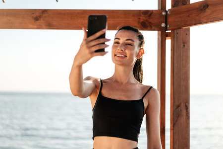 Image of beautiful young pretty fitness woman outdoors at the beach using mobile phone