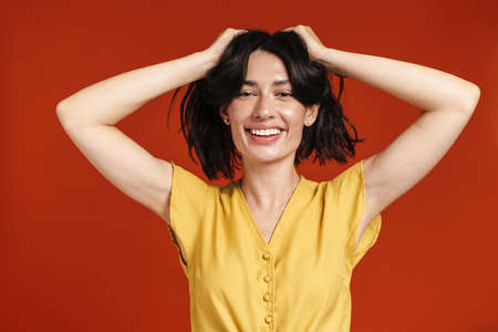 Image of young cheerful woman smiling and grabbing her head isolated over red backgroundの写真素材