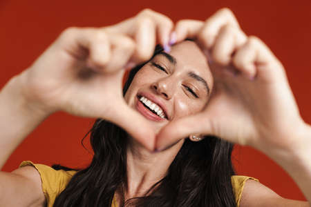 Image of caucasian smiling woman making heart gesture isolated over red background