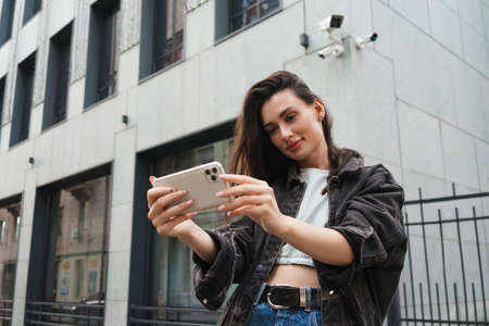 Image of concentrated young woman walking outdoors by the street and using mobile phoneの写真素材