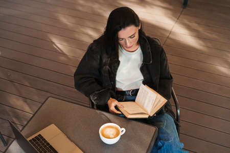 Image of concentrated pretty young woman sitting in cafe and using laptop computer while drinking...