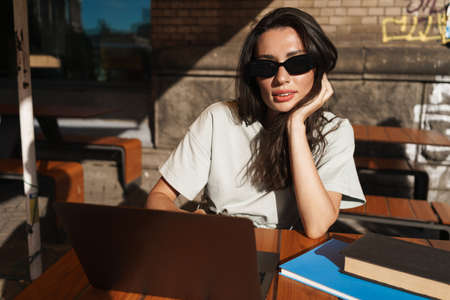 Image of beautiful concentrated young woman in cafe outdoors using laptop computerの写真素材