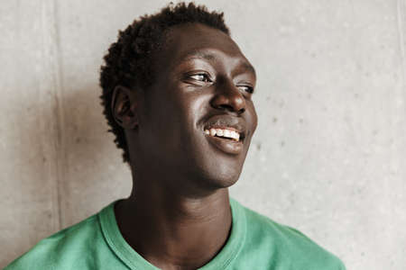Image of attractive happy young african american man in casual clothes smiling and looking aside...