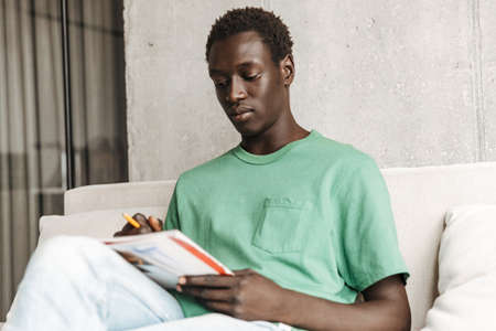 Image of brunette handsome african american man in casual clothes studying with exercise books at...