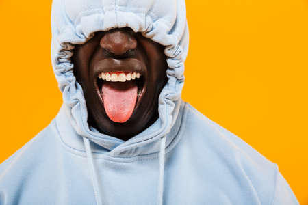 Image of funny african american guy in streetwear hoodie sticking out his tongue isolated over...