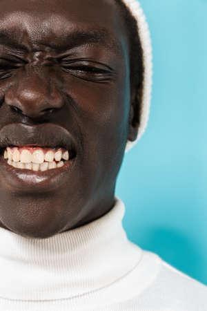 Image closeup of joyous african american guy in white clothes smiling at camera isolated over blue...