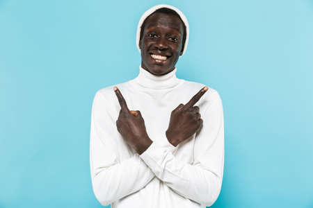 Image of happy african american guy in white clothes smiling and pointing fingers aside at copyspace...